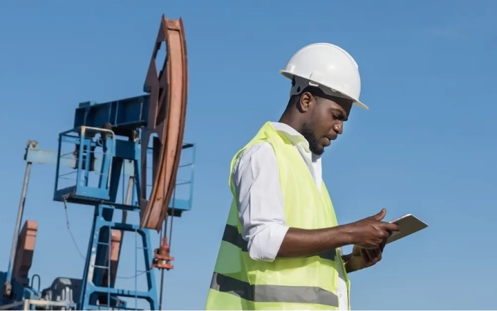 man looks at ipad in front of oil derrick